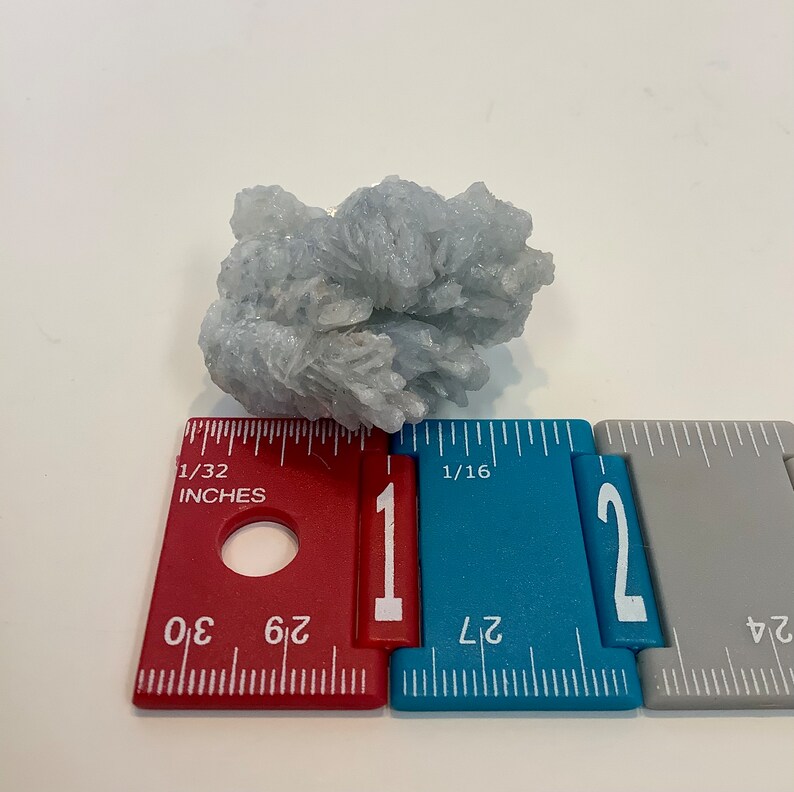Pu&ograve; includere: Un ammasso di cristalli blu chiaro che misura circa 2,5 cm di diametro. Il cristallo &egrave; su un righello con segni in pollici.