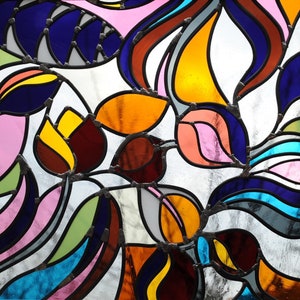 Könnte beinhalten: Ein farbenfrohes Buntglasfenster mit einem abstrakten floralen Design. Das Kunstwerk zeigt eine Vielzahl von Formen und Farben, darunter Blau, Orange, Gelb, Rosa und Grün, alle mit dunklem Metall umrandet.