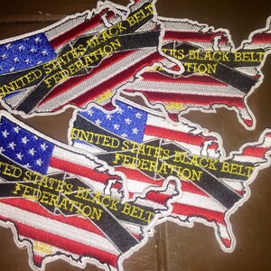 May include: Three embroidered patches in the shape of the United States of America. Each patch features a black and white striped ribbon across the American flag with the text "United States Black Belt Federation" in yellow.