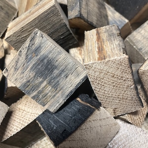 May include: A close-up of a pile of small, charred wood chips. The chips are various shades of brown and black, with some showing signs of charring. The chips are likely used for smoking food.