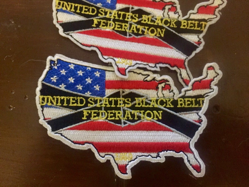 May include: Two embroidered patches in the shape of the United States of America. The patches are red, white, and blue with a black ribbon across the middle. The ribbon has the text "United States Black Belt Federation" in yellow lettering.