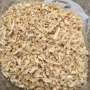 May include: A close-up of a clear plastic container filled with a large amount of light brown wood shavings. The shavings are very fine and appear to be uniform in size.