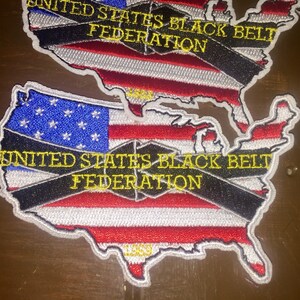 May include: A red, white, and blue embroidered patch shaped like the United States of America. The patch has a black belt across it with the text "UNITED STATES BLACK BELT FEDERATION" in yellow letters.