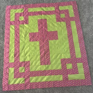May include: A green and pink patchwork quilt with a geometric design. The quilt is made of squares and rectangles, and the design is a series of intersecting lines.