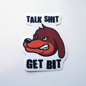 May include: A sticker featuring a cartoon dog with a red and brown head and the text "Talk Shit Get Bit" in black.