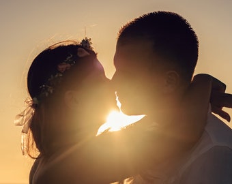 May include: Silhouette of a couple kissing at sunset, with the sun shining brightly behind them.