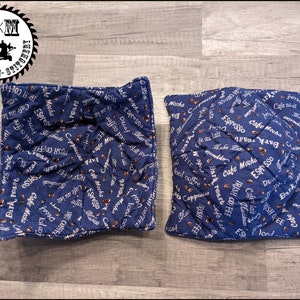 May include: Two blue quilted fabric squares with a coffee theme. The fabric has a white background with brown coffee beans and white text that says "Cafe Mocha", "Espresso", "Dark Roast", "Irish Coffee", "Cappuccino", and "Iced Coffee".