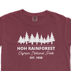 May include: A maroon t-shirt with a white graphic of a forest silhouette and the text "HOH RAINFOREST Olympic National Park EST. 1938"