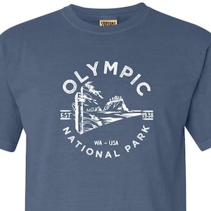 May include: A blue t-shirt with a white graphic of the Olympic National Park logo. The logo features a mountain range, trees, and the text "Olympic National Park Est. 1938 WA - USA".