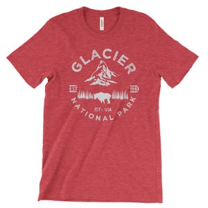 Peut inclure: T-shirt rouge en heather avec un motif blanc du parc national de Glacier, Montana, &Eacute;tats-Unis. Le motif comprend le nom du parc, une cha&icirc;ne de montagnes, un bison et les ann&eacute;es "EST 1910".