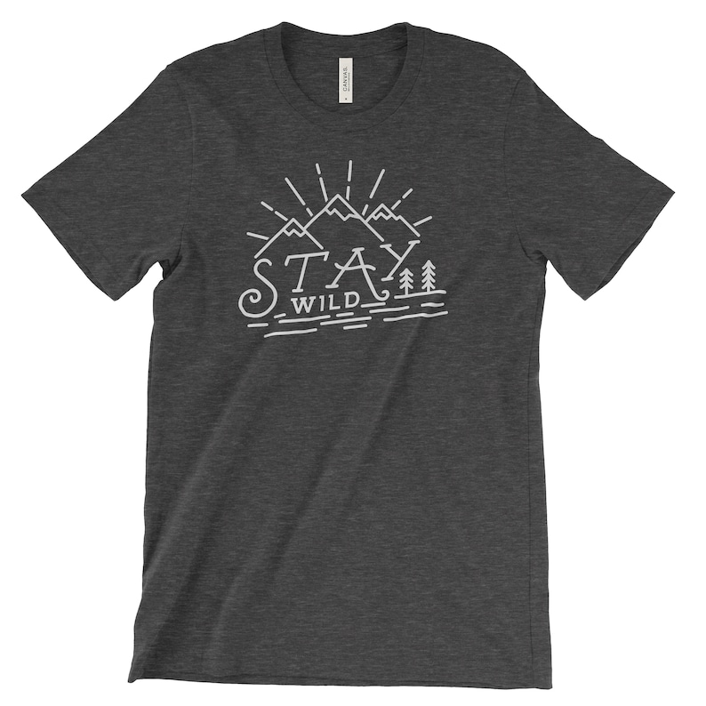 May include: Dark gray t-shirt with a white graphic design of mountains and trees. The text "Stay Wild" is printed below the mountains.