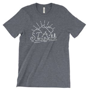 May include: A dark blue t-shirt with a white graphic design of mountains and trees. The text "Stay Wild" is printed below the mountains.