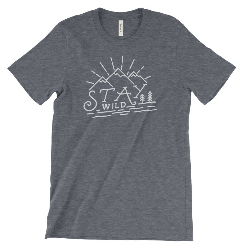May include: A dark blue t-shirt with a white graphic design of mountains and trees. The text "Stay Wild" is printed below the mountains.