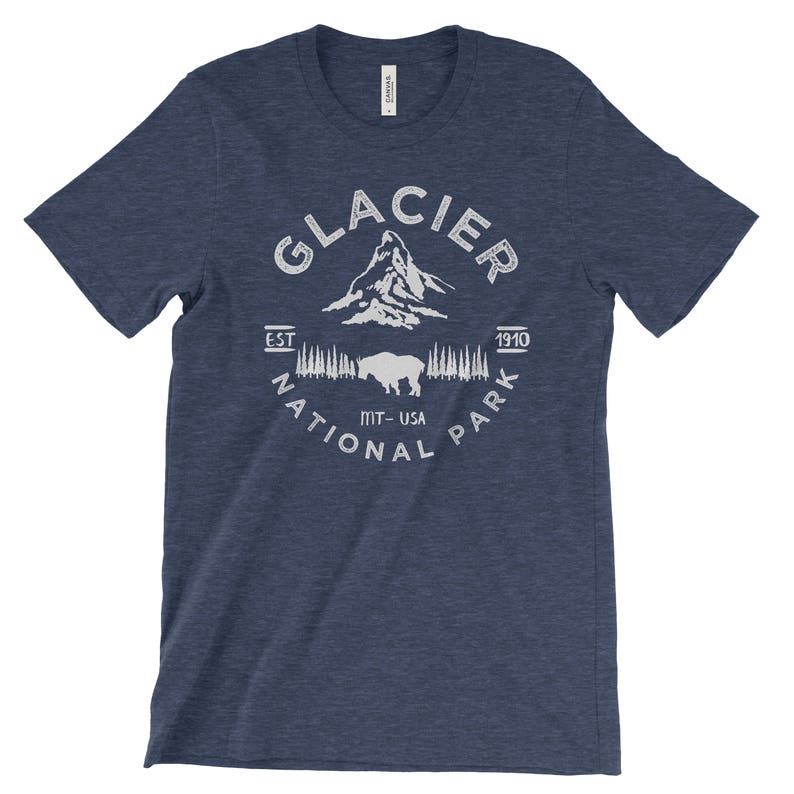 Peut inclure: Un t-shirt bleu marine avec un motif blanc du parc national de Glacier. Le motif comprend le nom du parc, une cha&icirc;ne de montagnes, un bison et le texte "Est. 1910, MT-USA, National Park".