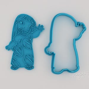 May include: Two blue plastic cookie cutters in the shape of a cartoon character. One cutter is a solid form, and the other is an outline. The character is waving with a smiling expression.