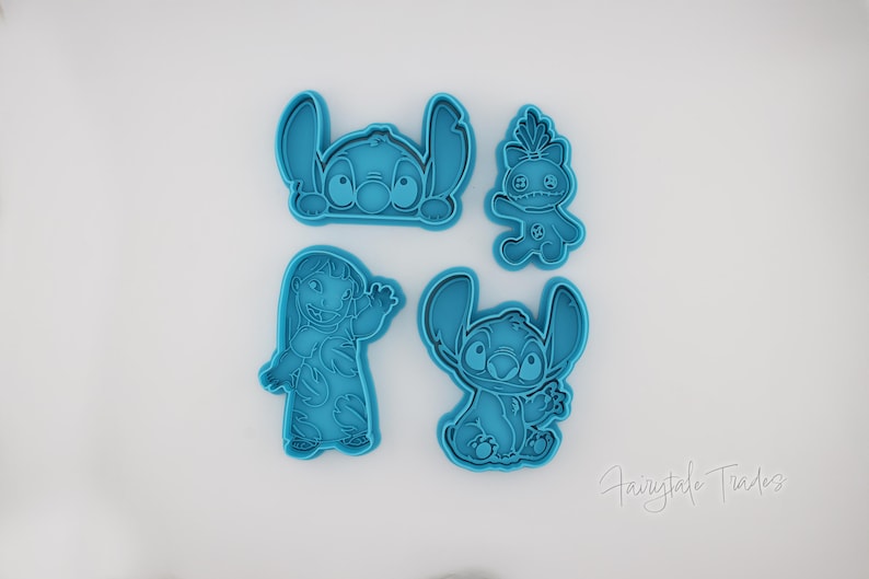 May include: Four teal-colored cookie cutters featuring characters from the animated film Lilo & Stitch. The cutters depict Stitch in various poses and a character named Angel. The cutters are made of plastic and are on a white background.