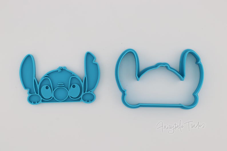 May include: Two blue plastic cookie cutters in the shape of the Disney character Stitch. One cutter is a detailed version of Stitch's face, and the other is an outline of the character's head. The cutters are on a white background.