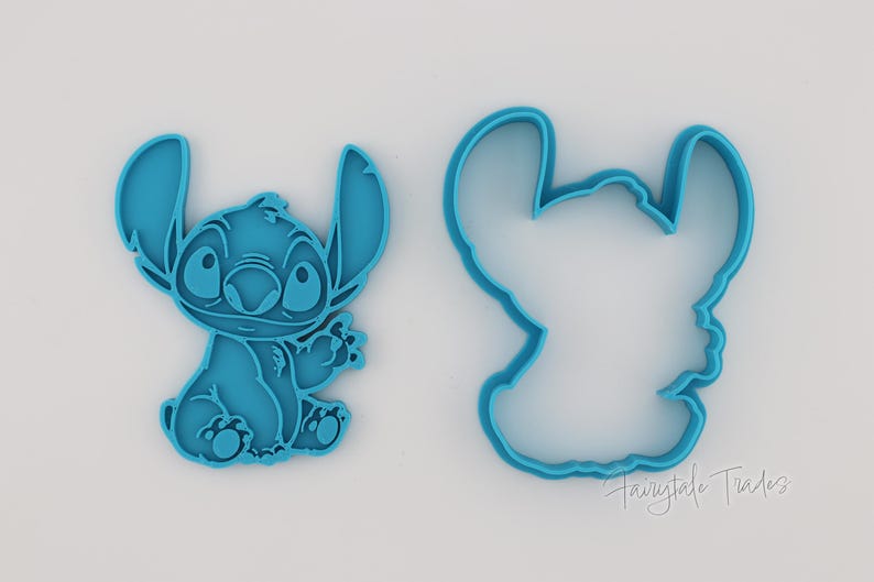 May include: Two teal-colored cookie cutters in the shape of the Disney character Stitch. One cutter is a solid figure of Stitch, and the other is an outline. The cutters are on a white background.