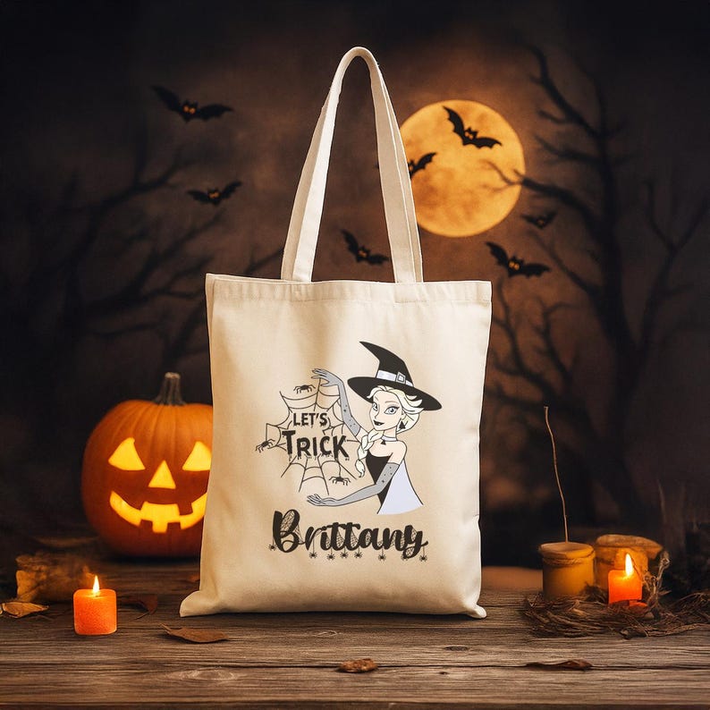 Op de afbeelding: Een cr&egrave;mekleurige draagtas met een Halloween-thema. Het ontwerp bevat een heksenillustratie, spinnenwebben en de tekst "Let's Trick" en "Brittany". De achtergrond toont een uitgesneden pompoen, kaarsen en een volle maan.