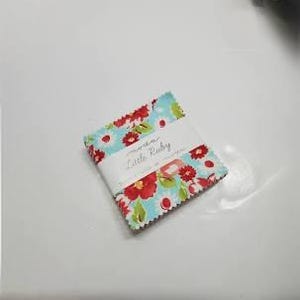 May include: A stack of fabric squares with a floral pattern in red, white, and green on a light blue background. The fabric is wrapped with a white label that reads "moda Little Ruby".