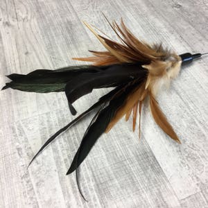 May include: A brown and black feather cat toy with a black plastic handle. The toy is designed to be used with a cat wand.