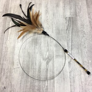 May include: A black and brown feather cat toy with a long, flexible wire wand. The wand has a black handle and a clear tube filled with black and gold glitter.