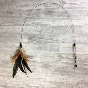 May include: A black and silver cat toy with a long, flexible wire and a feather and fur attachment. The toy is designed to be used interactively with a cat.