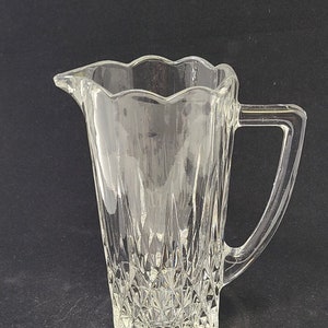 Könnte beinhalten: Eine klare Glaskaraffe mit Diamantenmuster und einem gewellten Rand. Die Karaffe hat einen Griff und ist perfekt zum Servieren von Getränken.