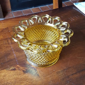 May include: A vintage, amber-colored glass dish with a diamond pattern and a decorative, scalloped rim. The dish is round and sits on a short base. The glass has a warm, golden hue.