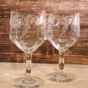 May include: Two clear glass wine glasses with etched floral designs. The glasses have a tall, slender stem and a wide bowl.