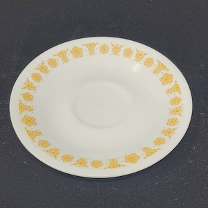 May include: A white saucer with a yellow floral pattern around the edge.
