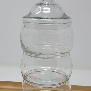 Pode incluir: Um frasco de vidro transparente com tampa, apresentando um design floral gravado. O frasco é dividido em três seções, perfeito para guardar pequenos objetos.