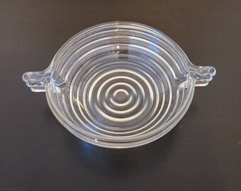 May include: A clear glass bowl with a concentric circle design and two handles. The bowl is made of glass and has a clear finish.