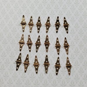 May include: A collection of eighteen small, gold-toned metal hinges arranged in three rows of six. Each hinge features a central cylindrical pivot point and two elongated, pointed plates with pre-drilled holes for mounting screws on both ends.