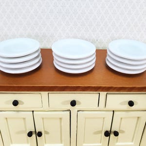 Pu&ograve; includere: Tre pile di quattro piccoli piatti rotondi bianchi disposti su una superficie in legno. Ogni pila &egrave; composta da piatti identici in ceramica bianca con una finitura liscia e un design circolare semplice, presentati in modo ordinato e pulito.