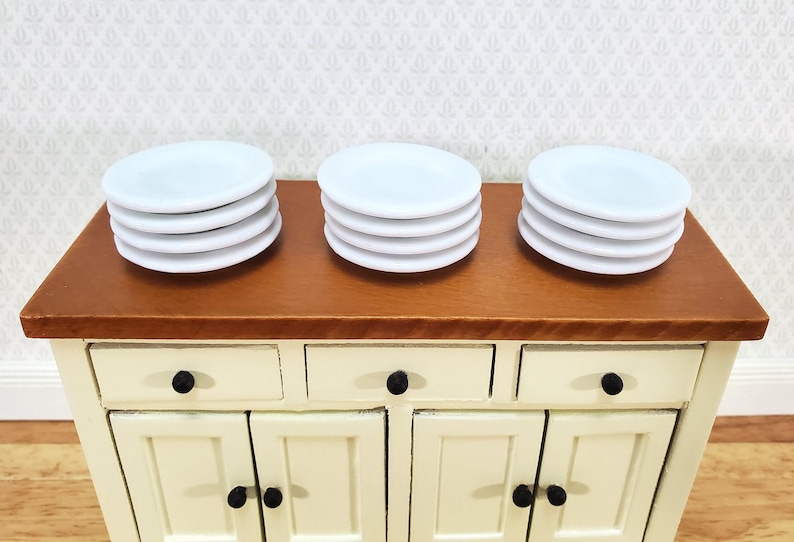 Pu&ograve; includere: Tre pile di quattro piccoli piatti rotondi bianchi disposti su una superficie in legno. Ogni pila &egrave; composta da piatti identici in ceramica bianca con una finitura liscia e un design circolare semplice, presentati in modo ordinato e pulito.