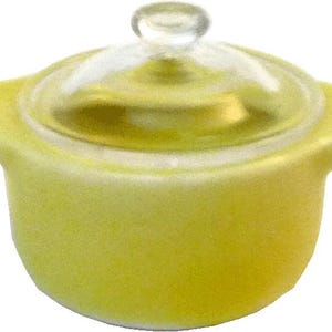 May include: A miniature yellow ceramic casserole dish with a clear glass lid and a small handle. The dish has two side handles and a clear knob on top of the lid. The overall design is simple and classic, suitable for a dollhouse or miniature kitchen.