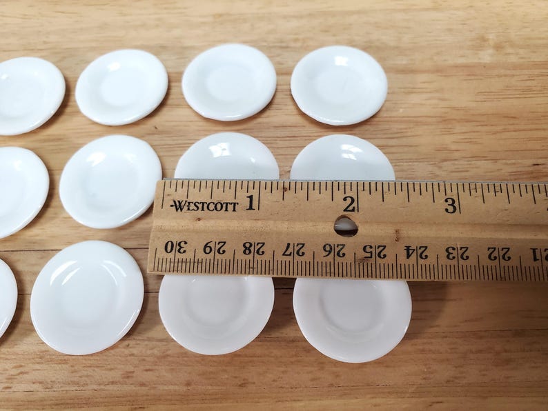 Pu&ograve; includere: Una collezione di piccoli piatti rotondi in ceramica bianca disposti in file. Un righello in legno Westcott &egrave; posizionato sopra i piatti, mostrando che ogni singolo piatto ha un diametro di circa 2,54 cm.
