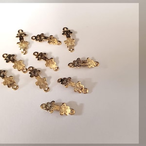 Könnte beinhalten: Eine Sammlung von neun kleinen goldfarbenen Metall-Schmuckverbindern. Jedes Teil weist ein zartes Blumenmuster mit einem geprägten Blumendesign in der Mitte und kleinen kreisförmigen Ösen an beiden Enden zur Befestigung an Ketten auf.