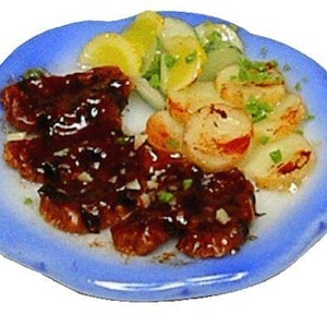 May include: A miniature plate of food featuring a dark brown, glazed meat dish, alongside sliced potatoes and a garnish of green herbs. The plate has a blue rim and a white center, creating a visually appealing presentation.