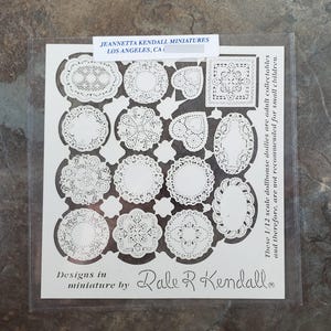 May include: A sheet of white paper with various miniature doily designs, including circles, hearts, and squares. The text "JEANNETTA KENDALL MINIATURES LOS ANGELES, CA" is printed at the top. The text "Designs in miniature by Dale R Kendall" is printed at the bottom.