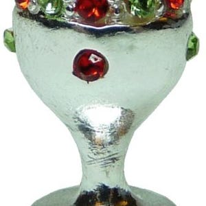 May include: Silver-colored goblet-shaped candle holder with a wide rim adorned with red and green jewels. A single red jewel is set on the body of the holder. The base is round.