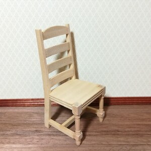 May include: A miniature wooden chair with a ladder back and a square seat. The chair is unfinished, showing the natural wood grain. The chair's dimensions are approximately 6.35 cm tall.