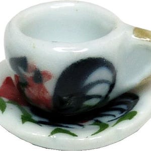 May include: A miniature white ceramic teacup and saucer set. The cup and saucer are decorated with a rooster design in black, red, and green. The handle of the cup has a gold accent. The saucer has a scalloped edge.