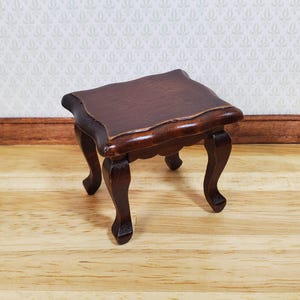 May include: A miniature dark brown wooden table with a scalloped edge and curved legs. The table has a rich, glossy finish, and is designed for a dollhouse or miniature setting.