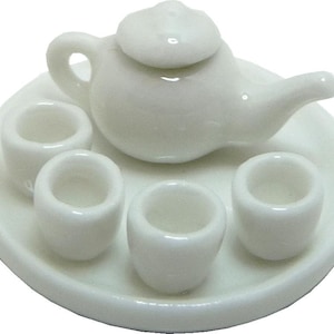 May include: A miniature white ceramic tea set, including a teapot with a lid, three small cups, and a round serving tray. The set is designed with smooth, glossy surfaces, perfect for a dollhouse or decorative display.