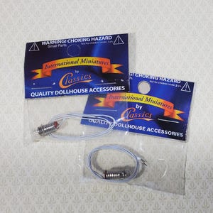 May include: Miniature dollhouse accessories, including small light bulbs with red tips and blue and white wires, packaged with warning labels. The labels read "WARNING! CHOKING HAZARD" and "International Miniatures by Classics".