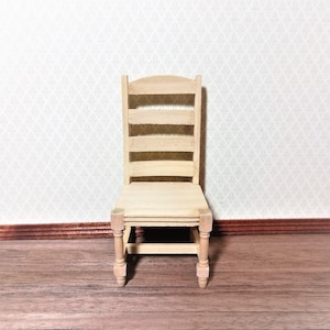 May include: A miniature wooden chair with a ladder back design. The chair is unfinished, showing the natural wood grain. The seat and legs are also made of wood. The chair is set against a patterned wallpaper background and a wooden floor.