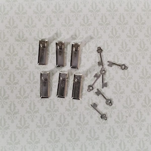 以下が含まれることがあります： 小さな銀色の金属製留め具とミニチュアのスケルトンキーのコレクション。留め具は長方形で上部が円形、キーは複雑なデザインです。アイテムは、模様のある明るい色の表面に散らばっています。