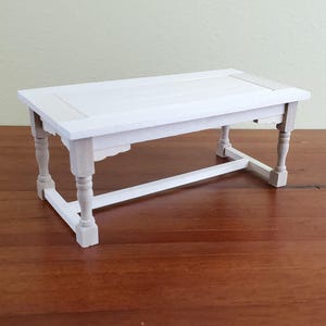 Op de afbeelding: Een kleine, witte houten tafel met een rechthoekig blad en gedraaide poten. De tafel is ongeveer 30 cm lang, 15 cm breed en 15 cm hoog. De tafel is wit geschilderd en heeft een eenvoudig, elegant ontwerp.